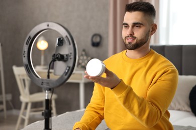 Beauty blogger reviewing cosmetic product and recording video with smartphone and ring lamp at home