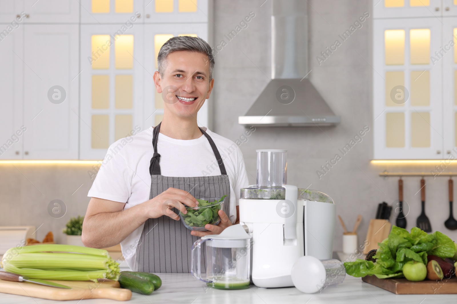 Photo of Smiling man with juicer and fresh products at white marble table in kitchen