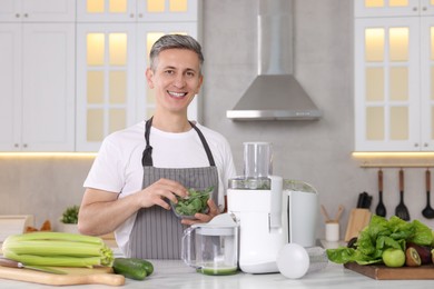 Smiling man with juicer and fresh products at white marble table in kitchen