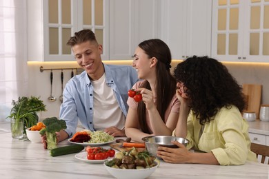 Photo of Friends cooking healthy vegetarian meal at white marble table in kitchen