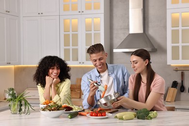 Friends cooking healthy vegetarian meal at white marble table in kitchen