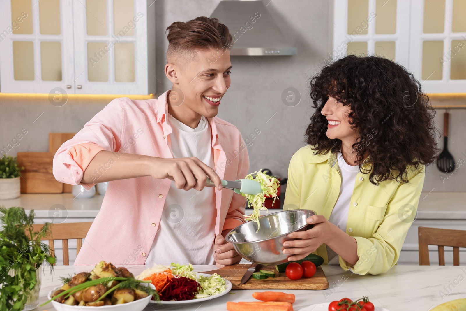 Photo of Friends cooking healthy vegetarian meal at white marble table in kitchen