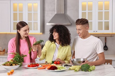 Photo of Friends cooking healthy vegetarian meal at white marble table in kitchen