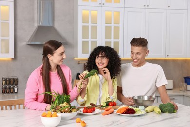 Photo of Friends cooking healthy vegetarian meal at white marble table in kitchen