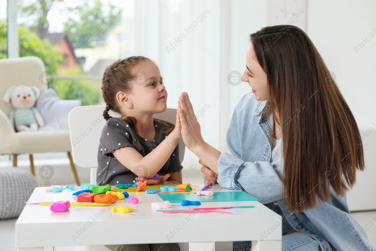 Photo of Play dough activity. Daughter giving five to her mother at table indoors