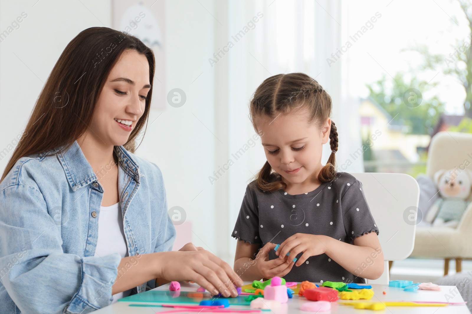 Photo of Smiling mother and her daughter sculpting with play dough at table indoors