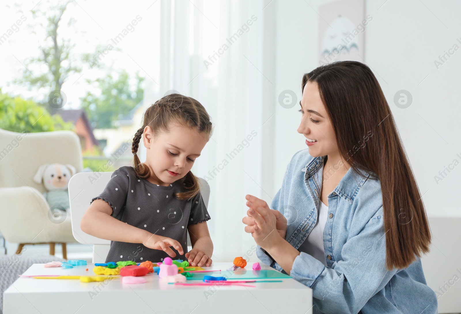 Photo of Smiling mother and her daughter sculpting with play dough at table indoors