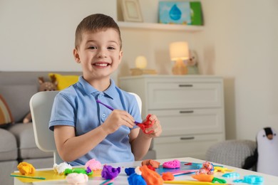 Photo of Smiling boy sculpting with play dough at table indoors