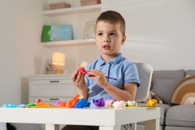 Little boy sculpting with play dough at table indoors