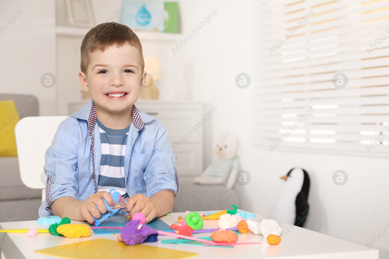 Photo of Smiling boy sculpting with play dough at table in kindergarten. Space for text