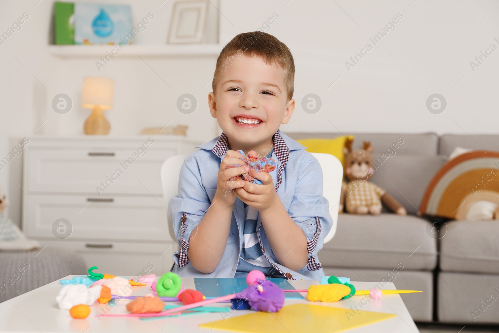 Photo of Smiling boy sculpting with play dough at table in kindergarten