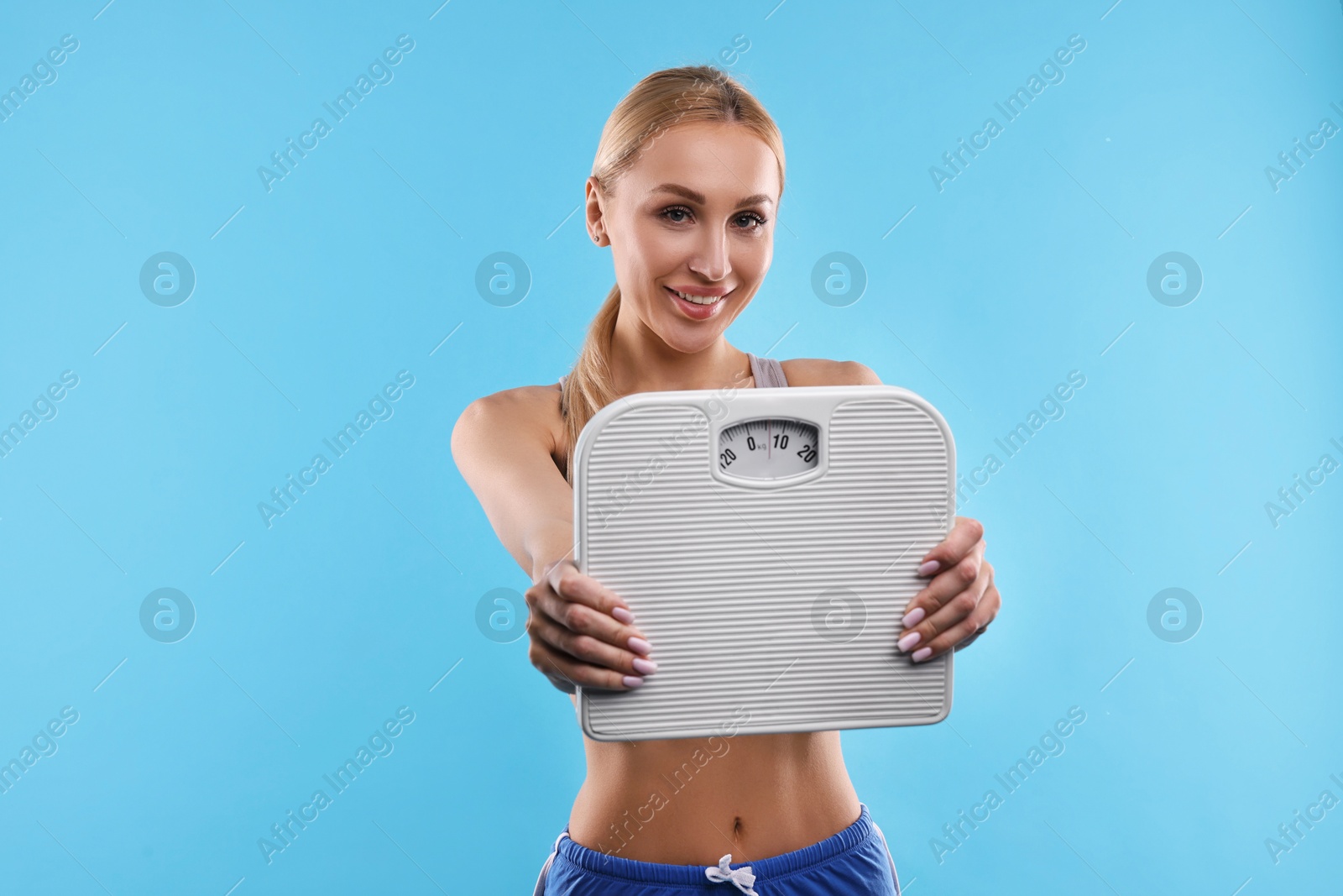 Photo of Happy woman with floor scale on light blue background