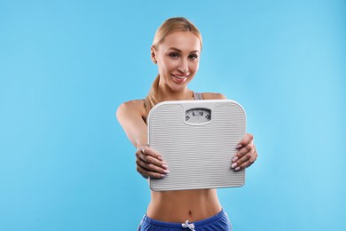 Happy woman with floor scale on light blue background