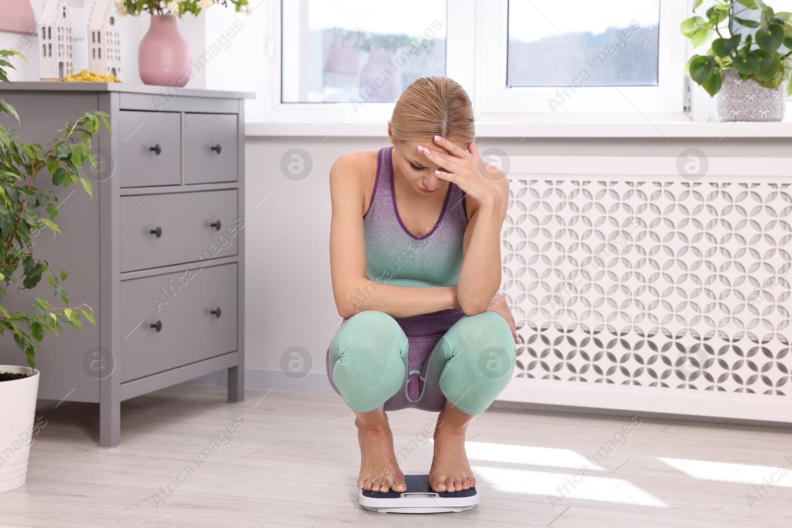 Photo of Worried woman on floor scale at home