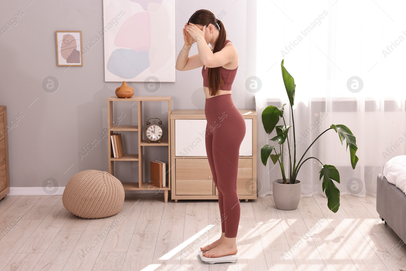 Photo of Worried woman standing on floor scale at home