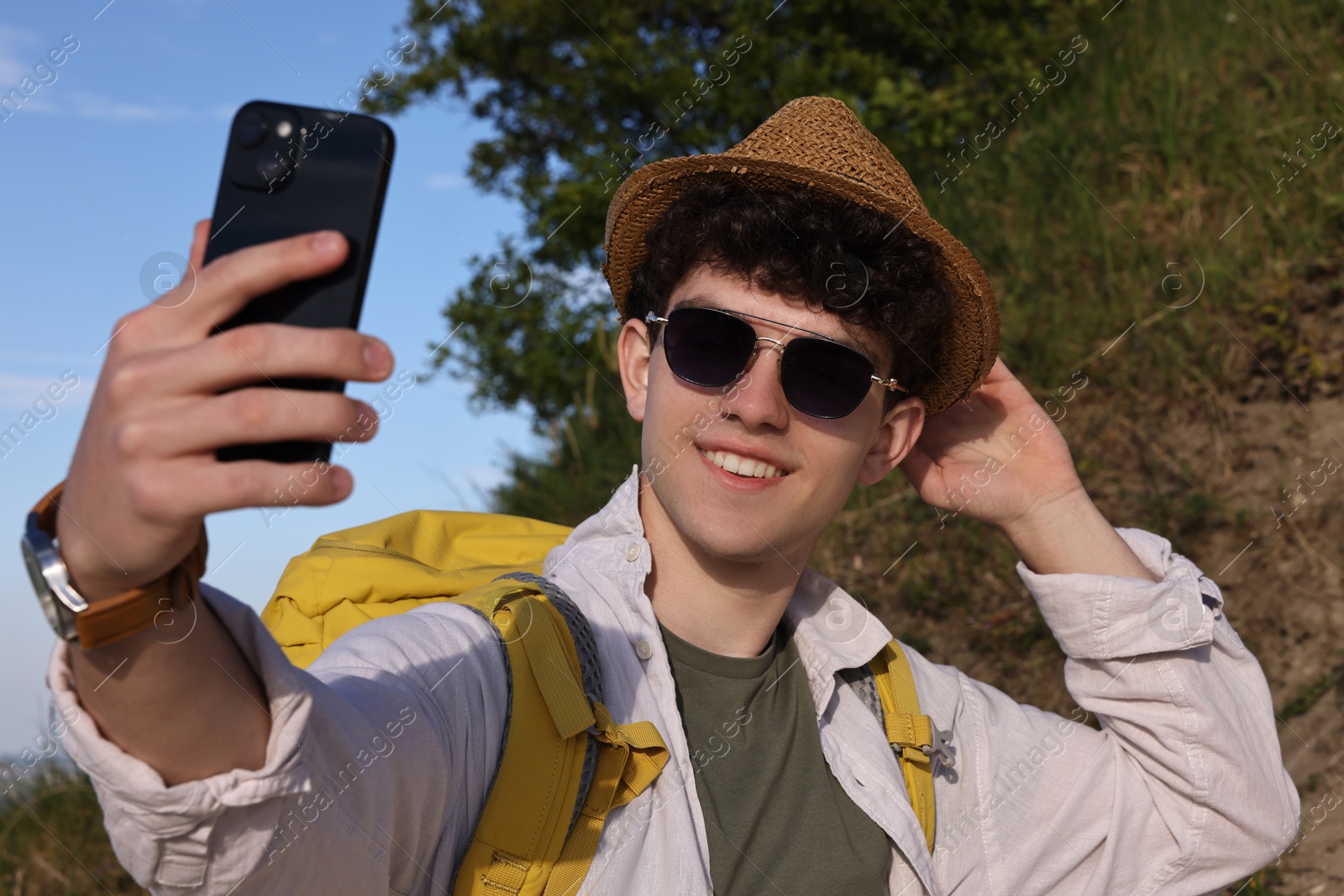 Photo of Travel blogger in sunglasses takIng selfie with smartphone outdoors