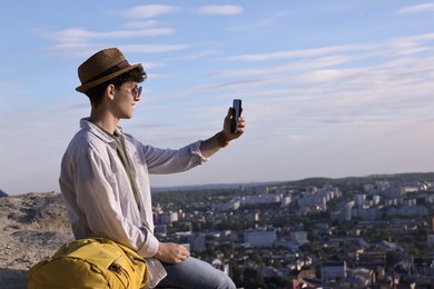 Travel blogger in sunglasses takIng selfie with smartphone outdoors, space for text