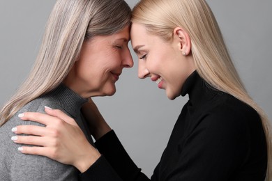 Family portrait of young woman and her mother on grey background