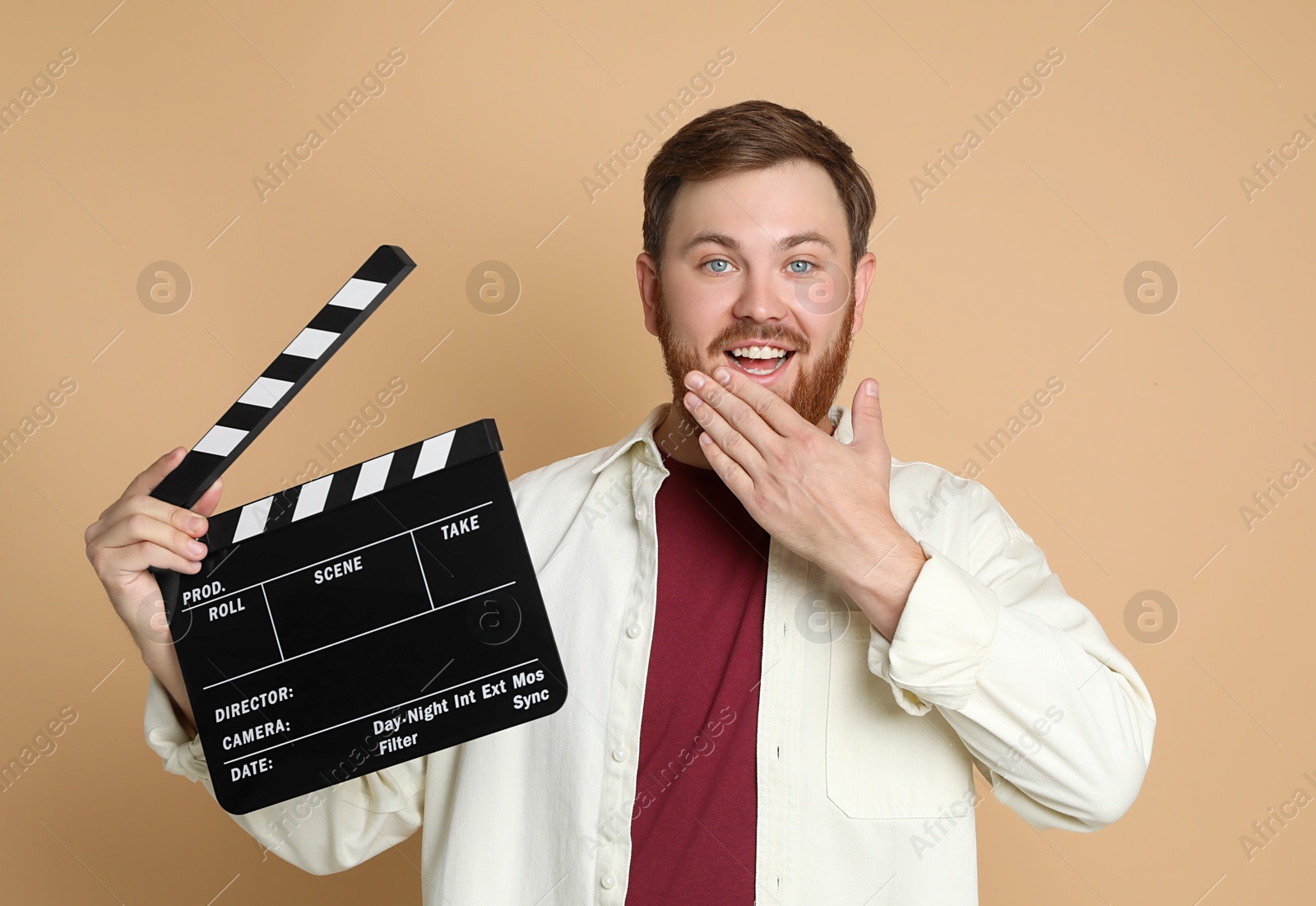 Photo of Making movie. Happy man with clapperboard on beige background
