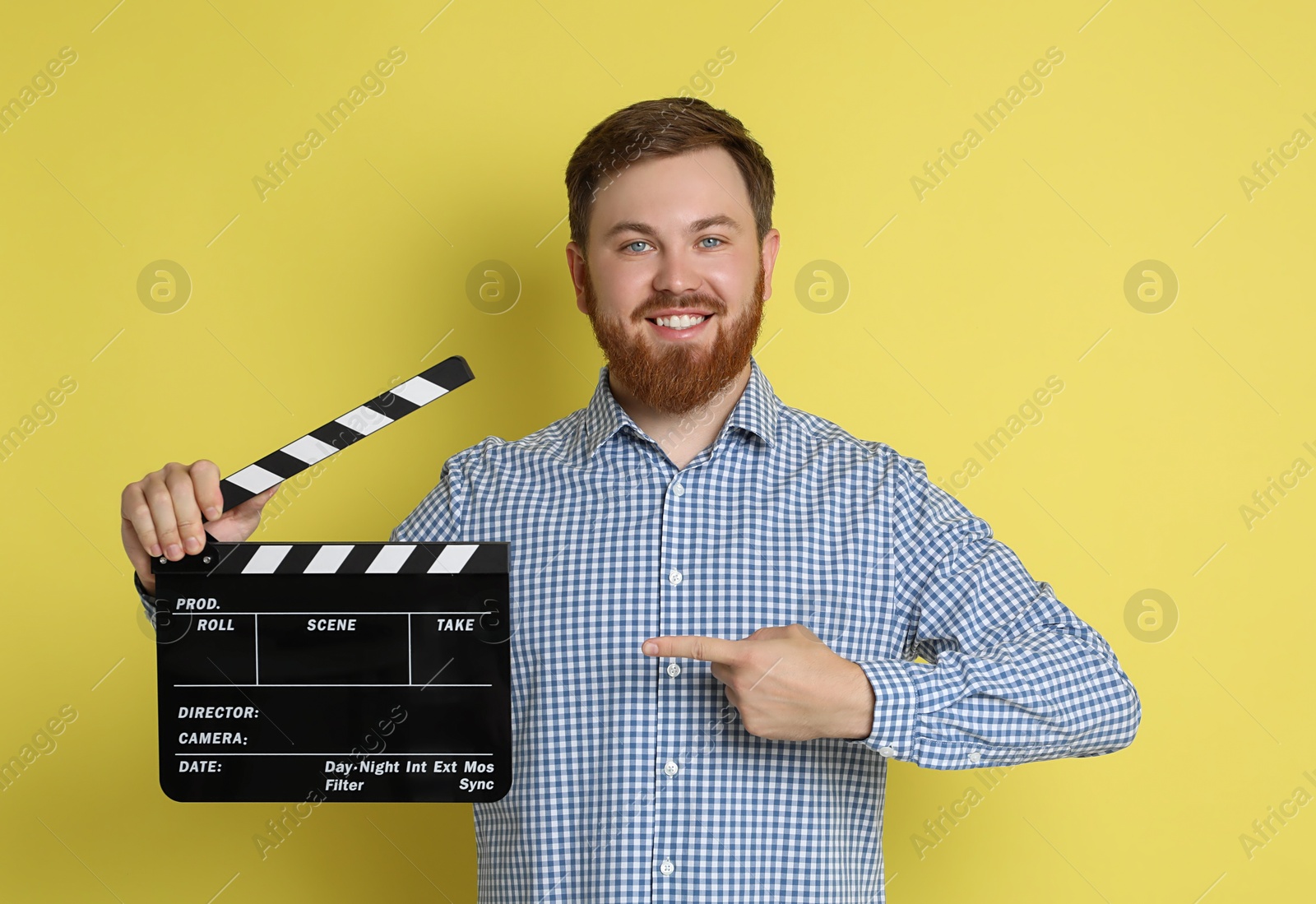 Photo of Making movie. Smiling man pointing at clapperboard on yellow background