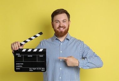 Making movie. Smiling man pointing at clapperboard on yellow background