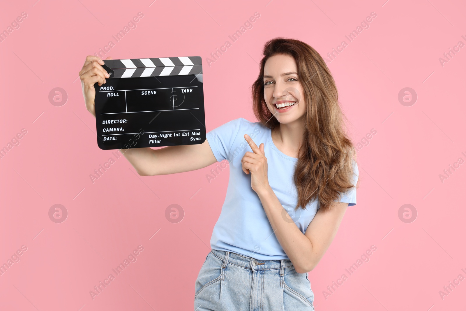 Photo of Making movie. Smiling woman pointing at clapperboard on pink background