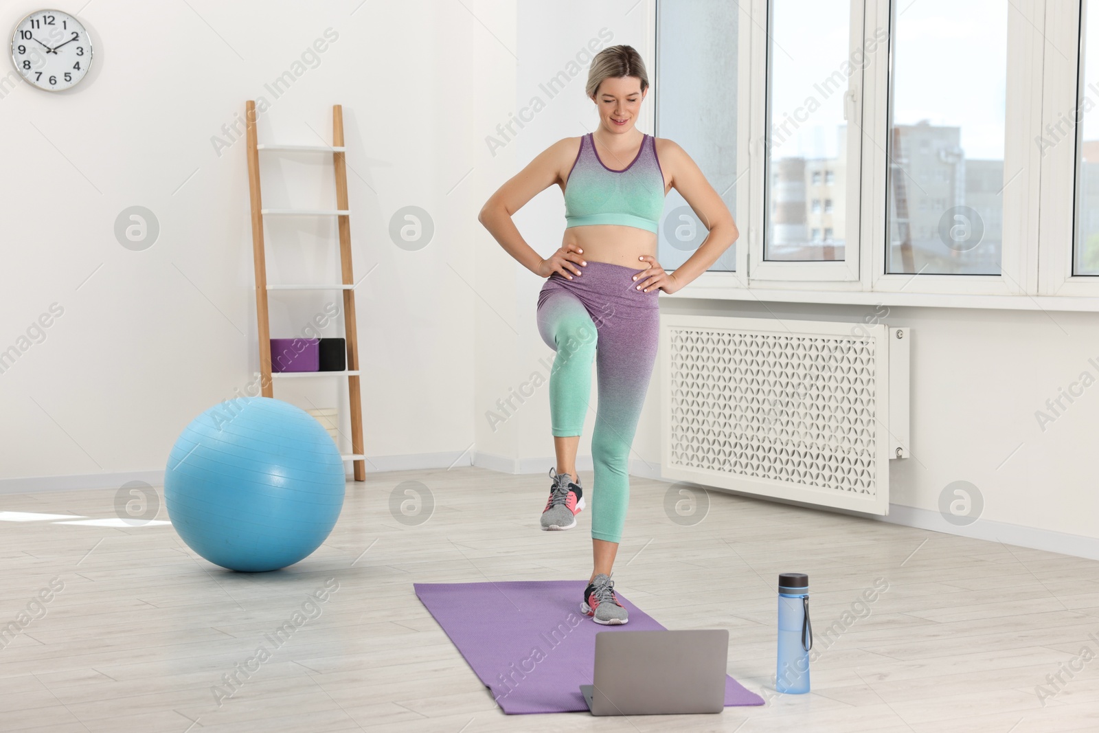 Photo of Online fitness trainer. Woman doing exercise near laptop at home