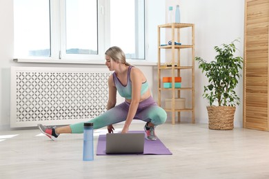 Photo of Online fitness trainer. Woman doing exercise near laptop at home