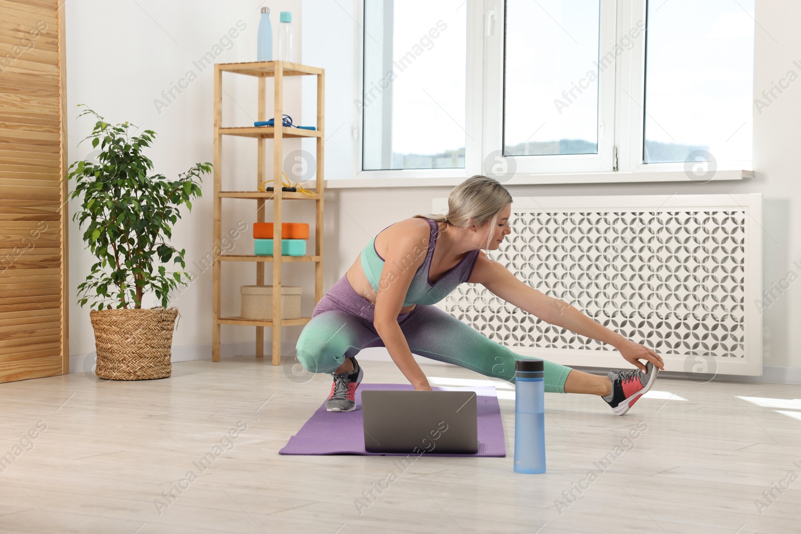 Photo of Online fitness trainer. Woman doing exercise near laptop at home