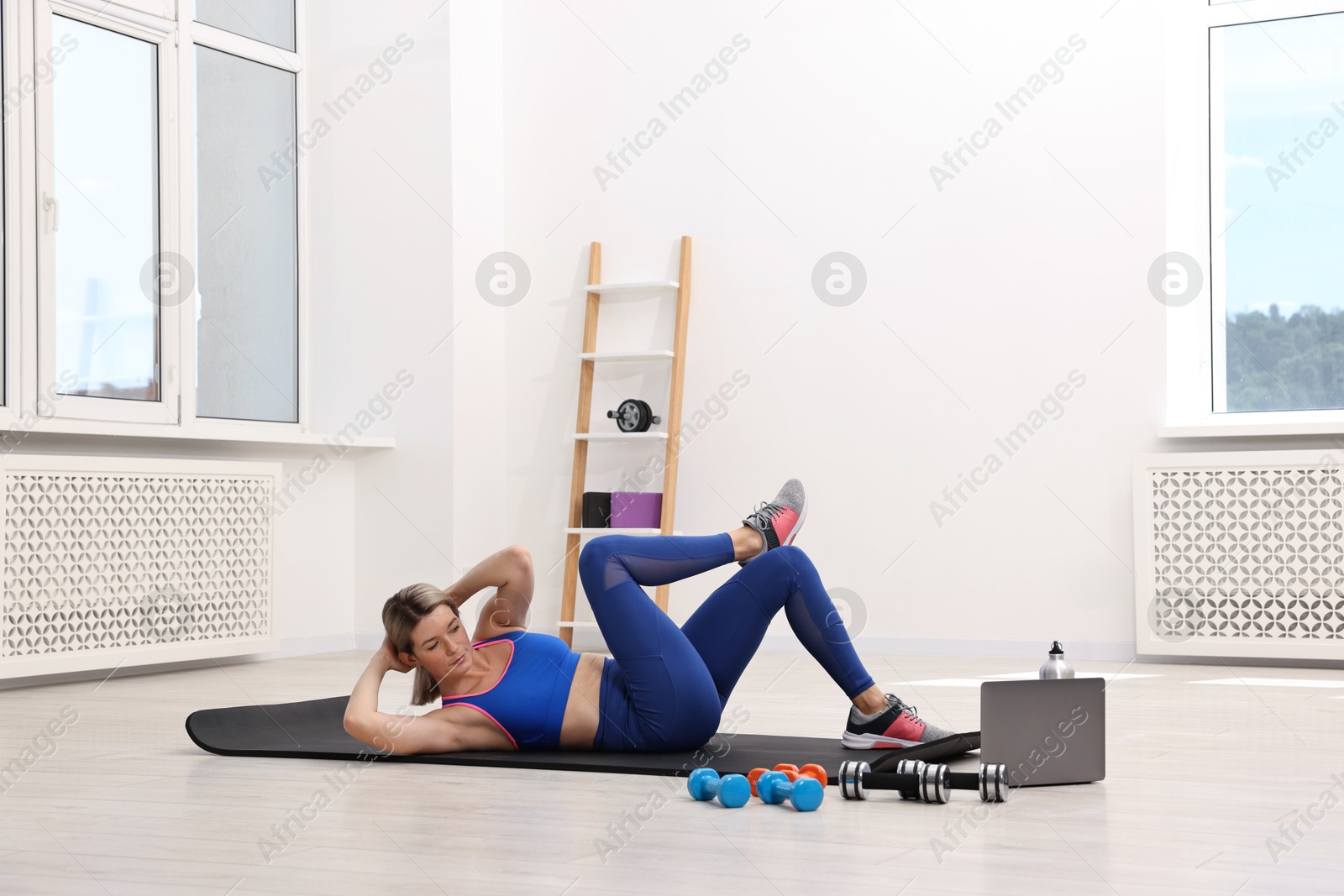 Photo of Online fitness trainer. Woman pumping up abs near laptop at home
