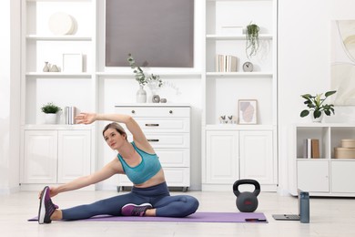 Photo of Online fitness trainer. Woman doing exercise near laptop at home