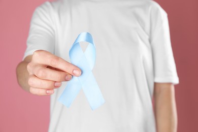 International Psoriasis Day. Woman with light blue ribbon as symbol of support on pink background, closeup