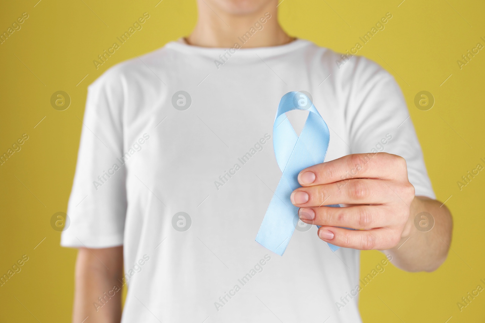 Photo of International Psoriasis Day. Woman with light blue ribbon as symbol of support on yellow background, closeup