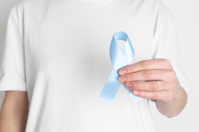 Photo of International Psoriasis Day. Woman with light blue ribbon as symbol of support on white background, closeup