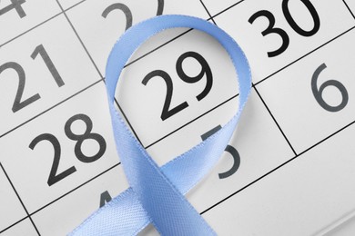 Photo of International Psoriasis Day. Light blue ribbon and calendar page with marked date, top view