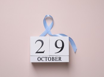 Photo of International Psoriasis Day - 29th of October. Block calendar and ribbon as symbol of support on beige background, top view