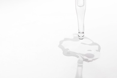 Photo of Glass pipette and transparent liquid on white background, closeup. Space for text