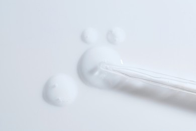 Photo of Glass pipette and transparent liquid on white background, top view