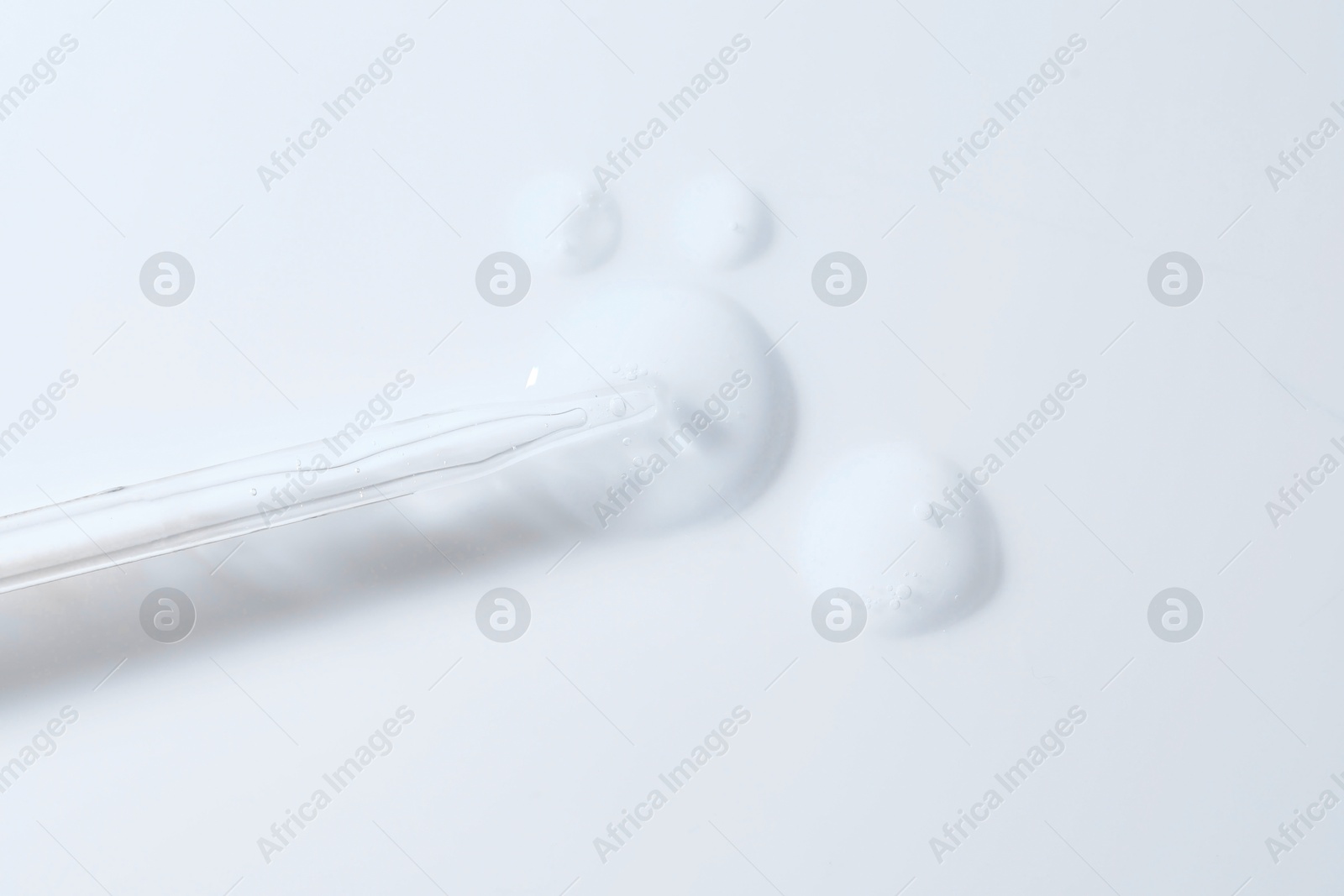 Photo of Glass pipette and transparent liquid on white background, top view
