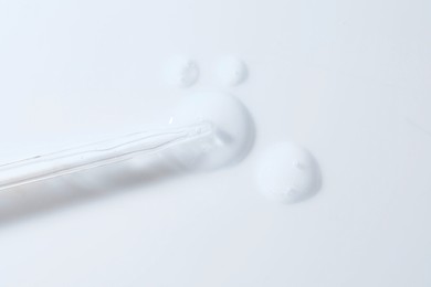 Glass pipette and transparent liquid on white background, top view