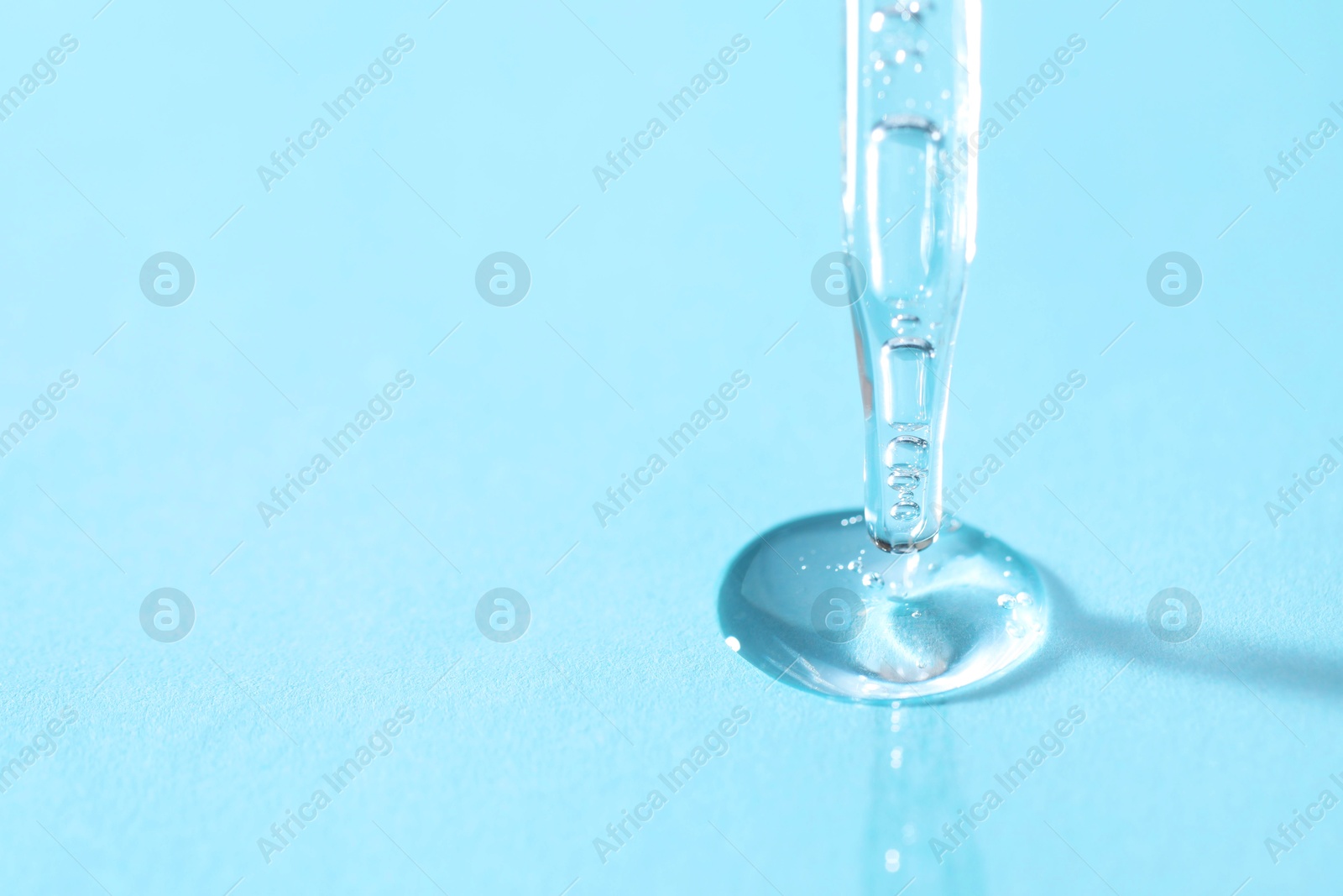 Photo of Glass pipette and transparent liquid on light blue background, closeup. Space for text