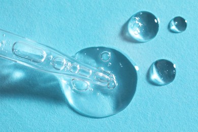 Glass pipette and transparent liquid on light blue background, top view