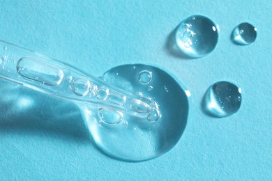 Photo of Glass pipette and transparent liquid on light blue background, top view