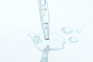Photo of Glass pipette and transparent liquid on light background, closeup