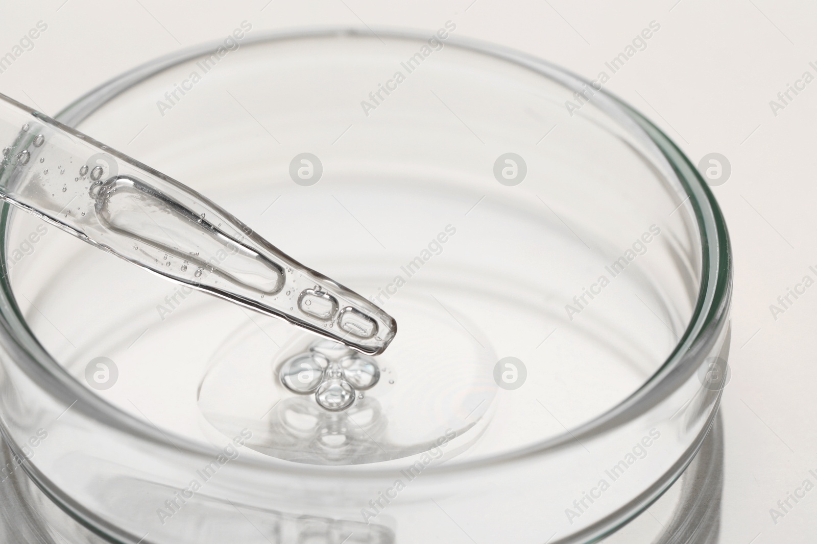 Photo of Glass pipette and petri dish with liquid on beige background, closeup