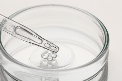 Glass pipette and petri dish with liquid on beige background, closeup