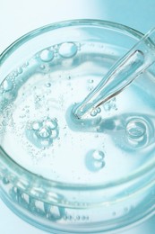 Photo of Glass pipette and petri dish with liquid on light blue background, closeup