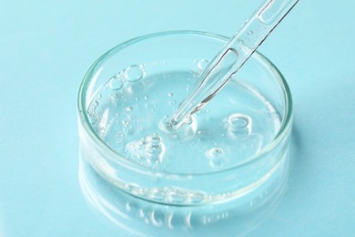 Photo of Glass pipette and petri dish with liquid on light blue background