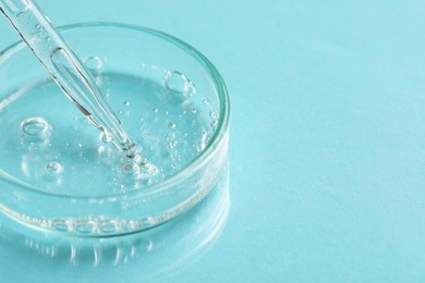 Glass pipette and petri dish with liquid on light blue background, closeup. Space for text