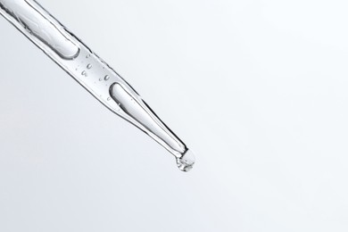 Photo of Dripping liquid from pipette on light blue background, closeup. Space for text